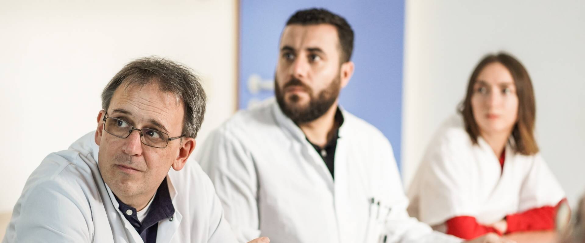 Zwei Ärzte, eine Ärztinnen an einem Tisch während einer Besprechung